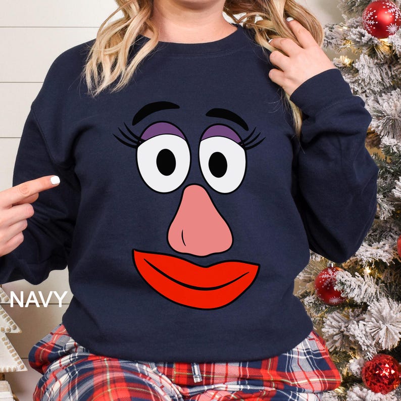 May include: Navy blue sweatshirt featuring a cartoon face with large white eyes, a pink nose, and a red mouth. The word "NAVY" is printed on the bottom left. The sweatshirt is part of a clothing collection.