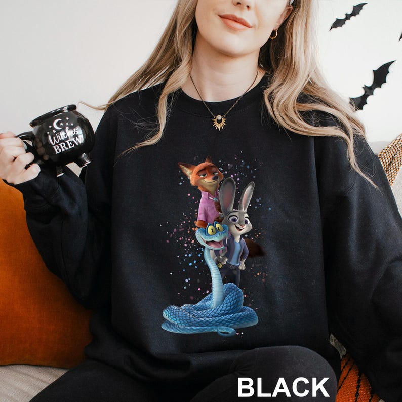 K&ouml;nnte beinhalten: Schwarzes Sweatshirt mit einer farbenfrohen Grafik von Zeichentrickfiguren, darunter ein Fuchs, ein Kaninchen und eine Schlange. Das Wort "BLACK" ist unten in Wei&szlig; aufgedruckt. Das Sweatshirt ist aus weichem Material.