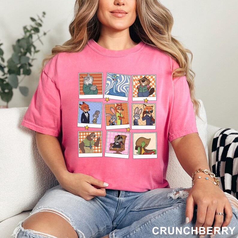 May include: A pink t-shirt featuring a grid of cartoon character images. The images are in a polaroid style with a star at the bottom. The text "CRUNCHBERRY" is at the bottom right of the shirt.