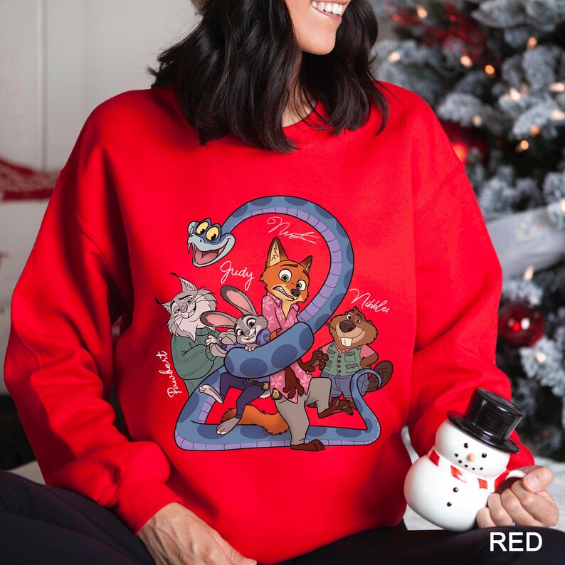 Op de afbeelding: Een rode sweatshirt met een cartoonillustratie van personages uit een film. Het ontwerp bevat een blauwe slang en de namen "Judy", "Nick" en "Nibbles". Het woord "RED" staat in het wit onderaan.
