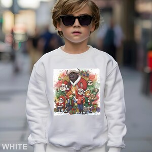 Op de afbeelding: Witte sweatshirt met een kleurrijke illustratie van stripfiguren in kerstoutfits, omringd door cadeaus. Een groot stierpersonage is verkleed als kerstman. Het woord "WHITE" staat onderaan.