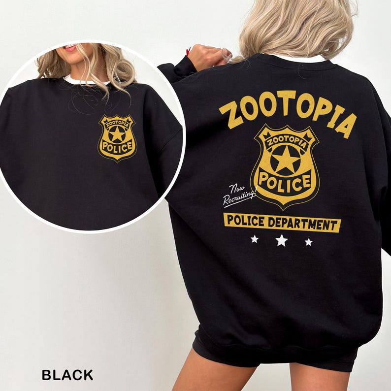 Puede incluir: Sudadera negra con una insignia dorada del Departamento de Polic&iacute;a de Zootopia en la parte delantera y trasera. El dise&ntilde;o trasero incluye el texto "Zootopia Police Department" y "Now Recruiting!" en dorado. La sudadera tiene un cuello blanco.
