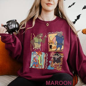 May include: Maroon sweatshirt featuring a colorful graphic of characters from the animated movie Zootopia. The design includes Judy Hopps, Nick Wilde, Flash, and Chief Bogo. The word "MAROON" is printed at the bottom of the sweatshirt.