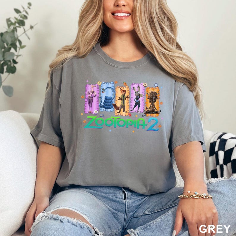 K&ouml;nnte beinhalten: Ein anthrazitfarbenes Kurzarm-T-Shirt mit einem Grafikdruck von f&uuml;nf animierten Charakteren aus Zootopia 2, die jeweils in einem bunten rechteckigen Rahmen dargestellt sind. Der Text Zootopia 2 ist in blauer Schrift unter den Figuren gedruckt.