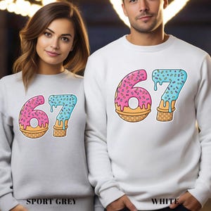 May include: Sport grey and white sweatshirts with a colorful graphic of the number 67 designed as a donut and ice cream cone. The number 6 is pink with sprinkles, and the 7 is blue with sprinkles. The text "SPORT GREY" and "WHITE" are at the bottom.