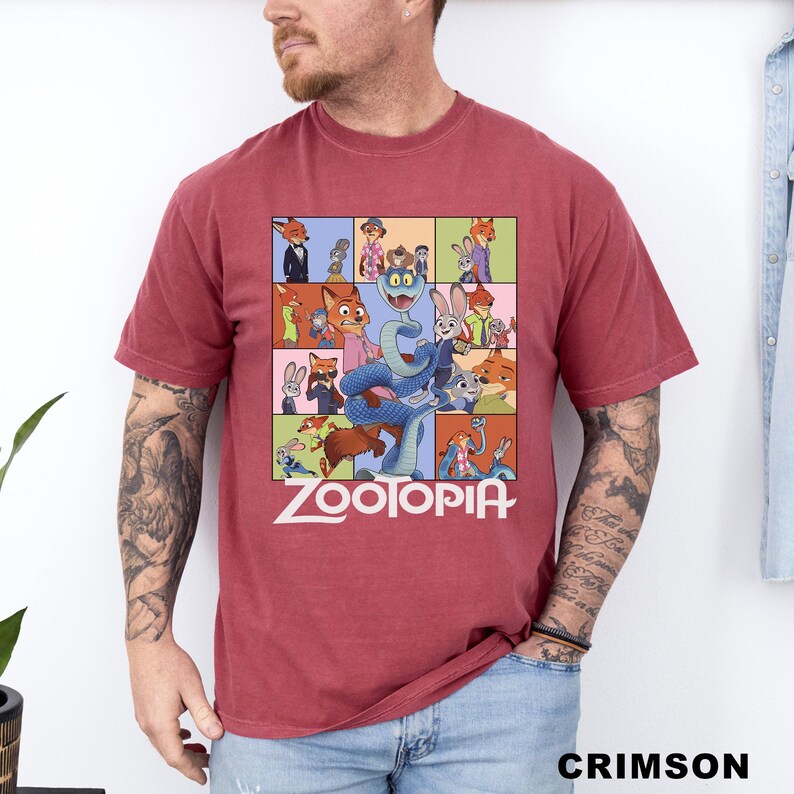 May include: Crimson-colored t-shirt featuring a colorful graphic from the animated movie "Zootopia." The design includes various characters from the film, with the title "Zootopia" in white block letters at the bottom. The shirt is a crew neck.