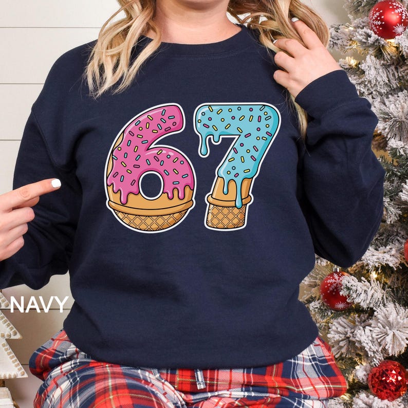 May include: Navy blue sweatshirt with a colorful graphic of the number 67 designed as a donut and ice cream cone. The number 6 is pink with sprinkles, and the 7 is blue with sprinkles. The word "NAVY" is printed on the bottom left.