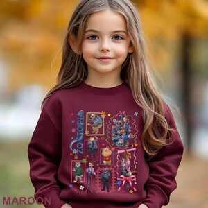 Puede incluir: Una sudadera granate con un dise&ntilde;o de Zootopia. El gr&aacute;fico incluye im&aacute;genes enmarcadas de varios personajes, incluyendo un perezoso y un grupo de perros. La palabra "Zootopia" est&aacute; escrita en una fuente decorativa. La palabra "MAROON" est&aacute; impresa en la parte inferior.