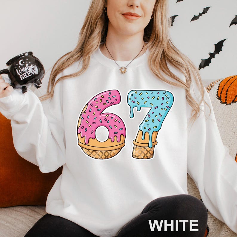 May include: White sweatshirt with a colorful graphic of the number 67, designed as donuts and ice cream cones. The number 6 is pink with sprinkles, and the 7 is blue with sprinkles. The word "WHITE" is printed at the bottom.
