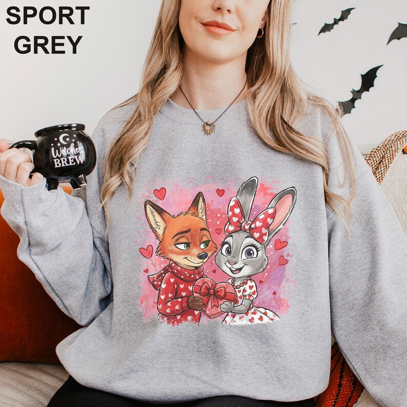 K&ouml;nnte beinhalten: Sportgraues Sweatshirt mit einem Cartoon-Fuchs und -Hasen, die eine herzf&ouml;rmige Geschenkbox halten, umgeben von Herzen. Der Fuchs tr&auml;gt einen roten Schal und der Hase hat eine rote Schleife. Der Text "SPORT GREY" steht oben.