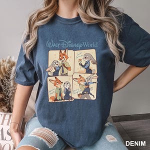 K&ouml;nnte beinhalten: Ein dunkelblaues T-Shirt mit Rundhalsausschnitt und einem Walt Disney World-Grafikdruck in vier Feldern, die die Zeichentrickfiguren Nick Wilde und Judy Hopps zeigen. Der Text umfasst Sweet Surrender, Adventure Awaits und Dancing Through Life.