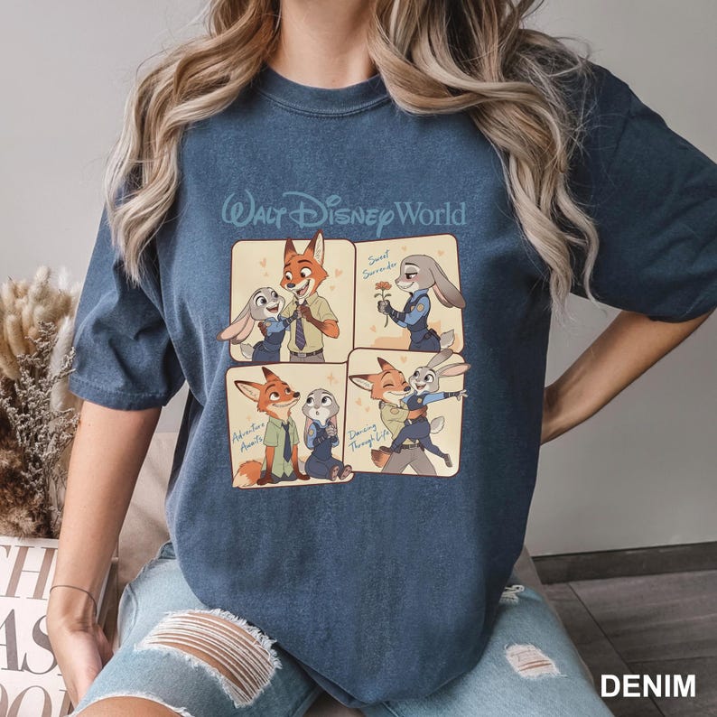K&ouml;nnte beinhalten: Ein dunkelblaues T-Shirt mit Rundhalsausschnitt und einem Walt Disney World-Grafikdruck in vier Feldern, die die Zeichentrickfiguren Nick Wilde und Judy Hopps zeigen. Der Text umfasst Sweet Surrender, Adventure Awaits und Dancing Through Life.