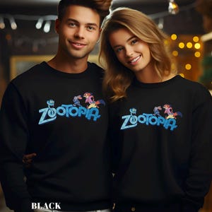 Puede incluir: Sudaderas negras con la palabra "Zootopia" en azul y personajes de dibujos animados. Las sudaderas son usadas por dos personas. La palabra "BLACK" est&aacute; impresa en la parte inferior de la imagen.