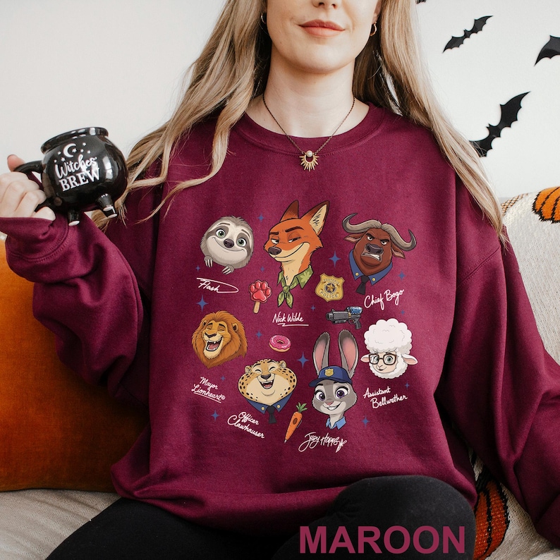 May include: Maroon sweatshirt featuring cartoon characters from Zootopia. The design includes Flash, Nick Wilde, Chief Bogo, Mayor Lionheart, Officer Clawhauser, Judy Hopps, and Assistant Bellwether. The word "MAROON" is printed at the bottom of the sweatshirt.
