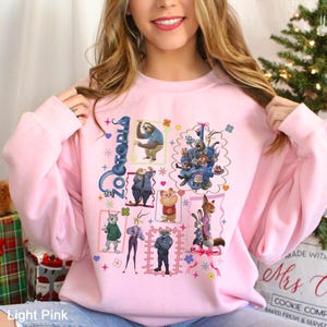 Puede incluir: Sudadera rosa claro con un gr&aacute;fico colorido de personajes de la pel&iacute;cula "Zootr&oacute;polis". El dise&ntilde;o incluye varios personajes de animales en ilustraciones enmarcadas, con la palabra "Zootr&oacute;polis" en una fuente estilizada. La sudadera es de color rosa claro.