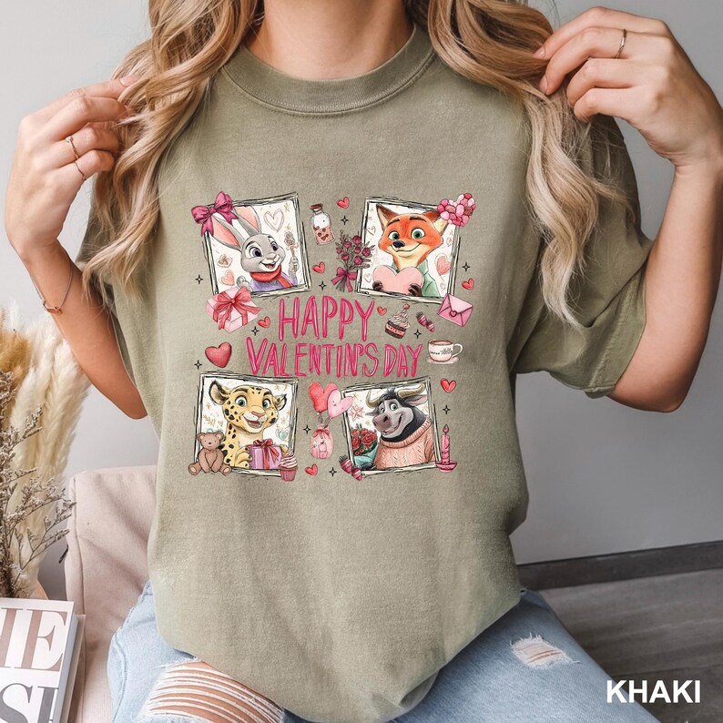 May include: Khaki-colored t-shirt featuring a Valentine's Day design with cartoon characters in framed portraits. The design includes the text "Happy Valentine's Day" with hearts and other decorative elements.
