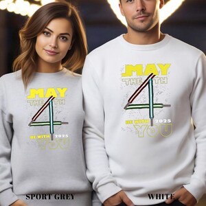 May include: Sport grey and white sweatshirts featuring the text "MAY THE 4TH BE WITH YOU 2025" in yellow. The design includes a stylized number 4 with lightsaber-like lines. The bottom of the sweatshirts read "SPORT GREY" and "WHITE".
