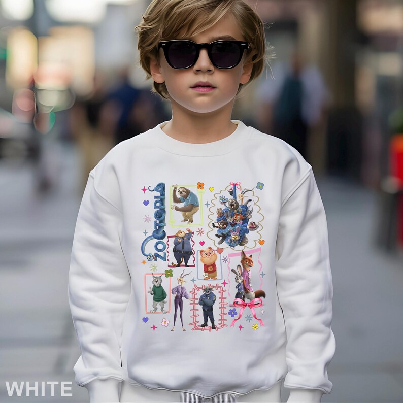Puede incluir: Sudadera blanca con un gr&aacute;fico colorido de personajes de la pel&iacute;cula animada "Zootopia". El dise&ntilde;o incluye varios personajes de animales en marcos rectangulares, con la palabra "Zootopia" en azul. La sudadera la lleva un ni&ntilde;o con gafas de sol.
