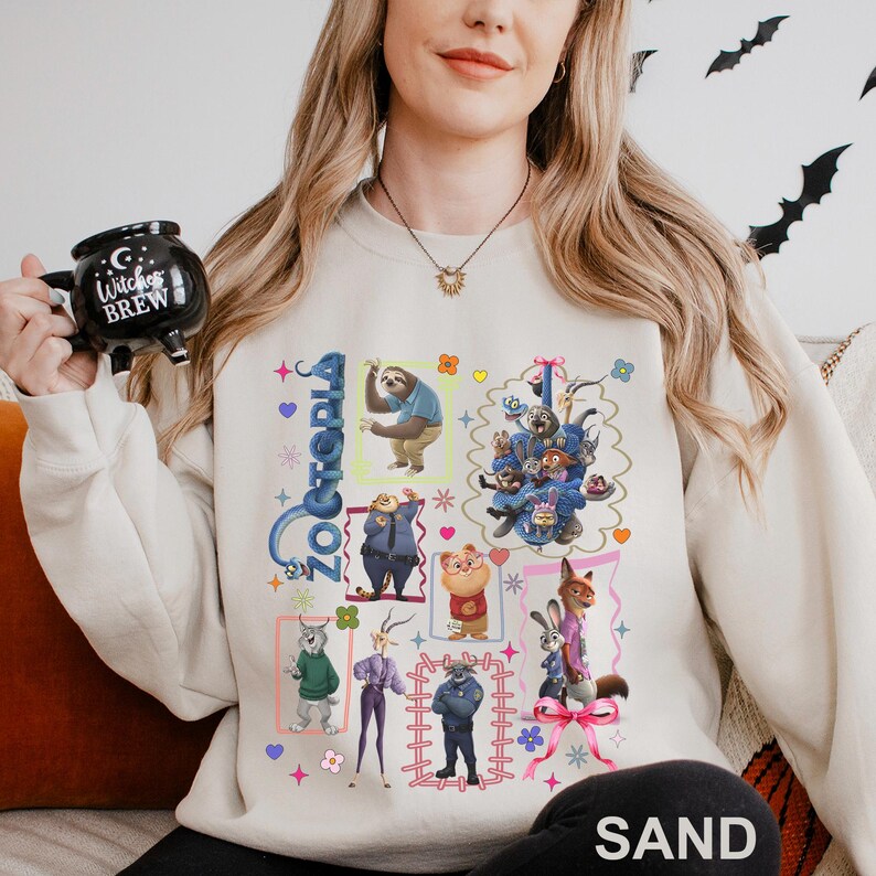 Puede incluir: Sudadera de color arena con un gr&aacute;fico colorido de personajes de la pel&iacute;cula animada "Zootopia". El dise&ntilde;o incluye varios personajes de animales en cuadros enmarcados, con la palabra "Zootopia" en una fuente estilizada. La palabra "SAND" est&aacute; impresa en la parte inferior.