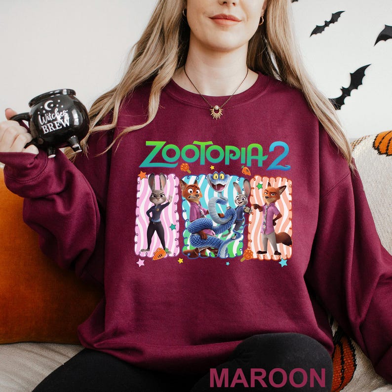 Puede incluir: Sudadera burdeos con cuello redondo con el texto "ZOOTOPIA 2" sobre un gr&aacute;fico de personajes de la pel&iacute;cula. El gr&aacute;fico incluye un conejo, un zorro y otros personajes. La palabra "MAROON" est&aacute; impresa en la parte inferior.