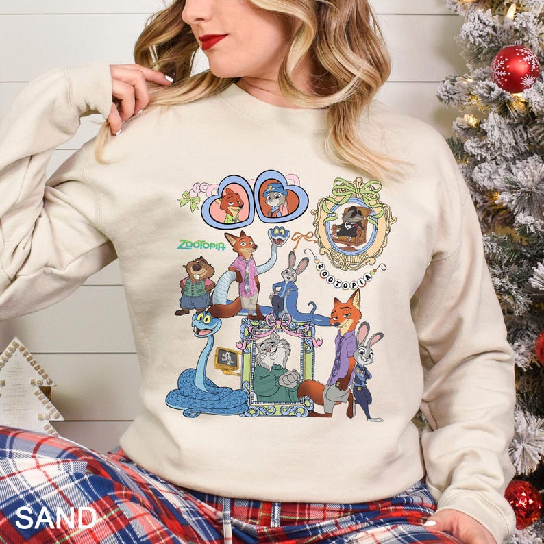 May include: Sand-coloured sweatshirt with a colourful graphic of characters from the animated film "Zootopia." The design includes various animal characters in frames and the word "Zootopia" in green. The sweatshirt has long sleeves.