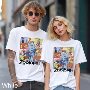 May include: White t-shirts featuring a colorful graphic from the animated movie Zootopia. The design includes various animal characters and the word "Zootopia" in black. The shirts are short-sleeved and worn by two people.