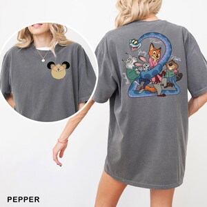 May include: A grey-green t-shirt with cartoon graphics. The front has a mouse character, and the back features a snake and cartoon characters. The names "Nick", "Judy", and "Nadia" are printed on the back. The word "Pepper" is at the bottom.