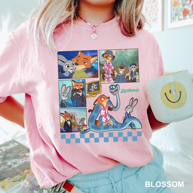 以下が含まれることがあります： 映画「ズートピア」のキャラクターが登場する漫画のデザインが施された、明るいピンク色のTシャツ。デザインにはキツネ、ウサギ、その他のキャラクターの画像が含まれています。「ズートピア」という言葉は緑色で印刷されています。黄色のスマイリーフェイスが付いた白いマグカップが持たれています。