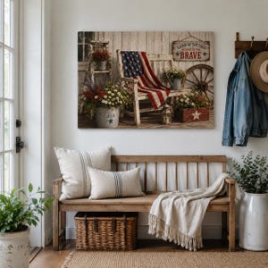 May include: A rustic wooden bench with two striped pillows and a woven basket. Above, a framed artwork depicts a patriotic scene with an American flag draped over a chair, flowers, and the text "Land of the Free Because of the Brave."