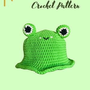 Peut inclure: Patron de chapeau seau en crochet de grenouille vert. Le chapeau a des yeux noirs avec un contour blanc. Le patron est de Clare Cox Crochet.