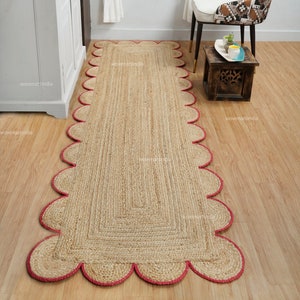 May include: A natural fiber rug with a scalloped edge and a pink trim. The rug is made of jute and is perfect for adding a touch of natural beauty to any room.