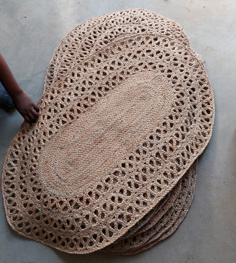 May include: A stack of oval-shaped jute rugs with a woven design. The rugs are a light brown colour and have a delicate, intricate pattern.