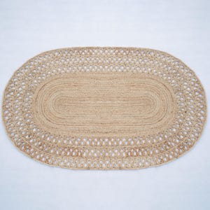 May include: An oval rug made from natural fibres, featuring a braided design and a decorative border. The rug is made of jute and has a light brown colour.