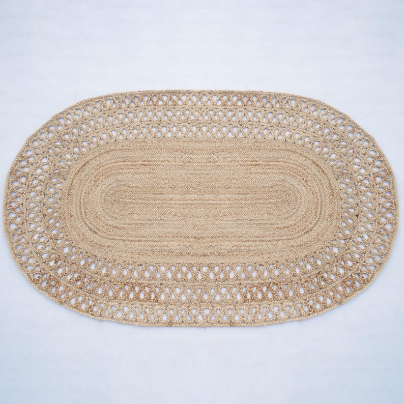 May include: An oval rug made from natural fibres, featuring a braided design and a decorative border. The rug is made of jute and has a light brown colour.