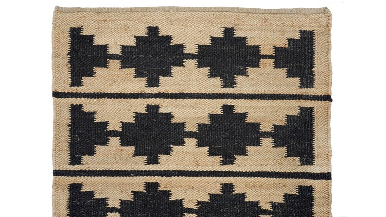 May include: A natural fiber rug with a geometric pattern in black and beige. The rug has a woven texture and a simple design.