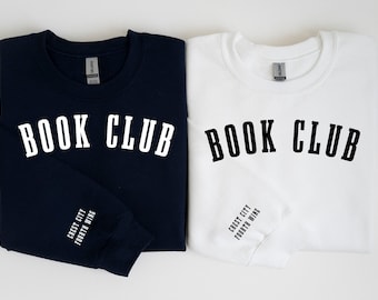 May include: Two sweatshirts with the text "BOOK CLUB" printed on the front. One sweatshirt is navy blue with white text and the other is white with black text. Both sweatshirts have the text "Crest City Fourth Wing" printed on the sleeve.
