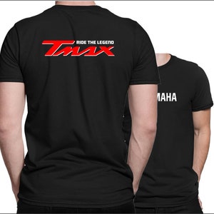 Op de afbeelding: Twee zwarte T-shirts met witte tekst. De voorkant van een shirt heeft de tekst "RIDE THE LEGEND" en een rood logo met de tekst "TMAX". De achterkant van het andere shirt heeft de tekst "YAMAHA" in wit.