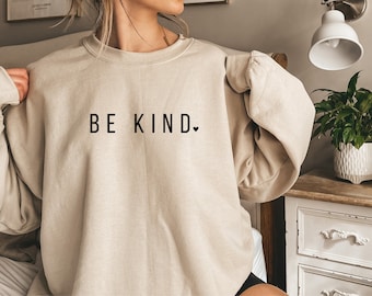 May include: A beige sweatshirt with the text "BE KIND." in black lettering and a small heart symbol.