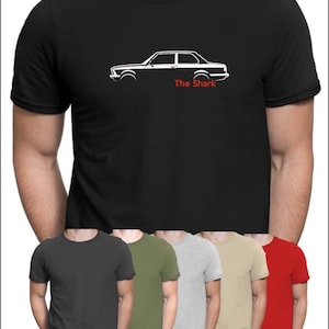 May include: A black t-shirt with a white silhouette of a car and the text "The Shark" printed on the front. The shirt is shown in a variety of colors, including black, gray, green, beige, and red.