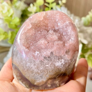 May include: A pink and white agate geode with a crystal-lined interior. The geode is smooth and polished, with a natural, irregular shape.
