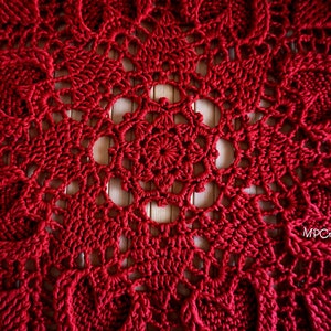 May include: A close-up of a red crocheted doily with a delicate, intricate pattern. The doily is made with a fine yarn and has a circular shape.