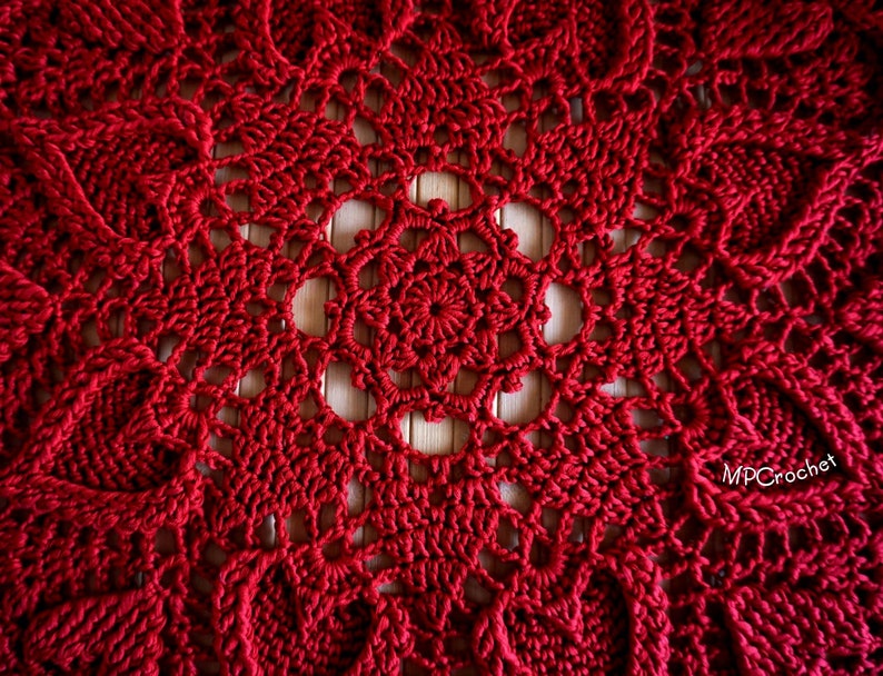 May include: A close-up of a red crocheted doily with a delicate, intricate pattern. The doily is made with a fine yarn and has a circular shape.