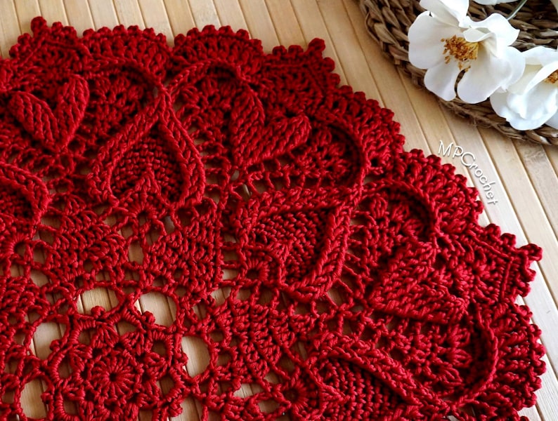 May include: A close-up of a red crocheted doily with a delicate floral pattern. The doily is made with a fine yarn and has a intricate design.