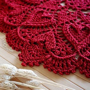 May include: A close-up of a red crocheted doily with a delicate, intricate design. The doily is made with a single crochet stitch and has a scalloped edge.