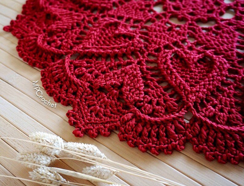 May include: A close-up of a red crocheted doily with a delicate, intricate design. The doily is made with a single crochet stitch and has a scalloped edge.