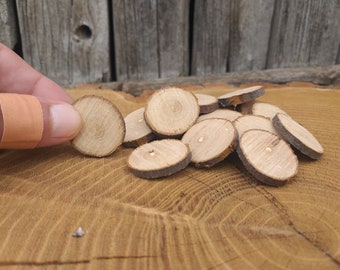 May include: A pile of small, round, wooden slices, with a natural wood grain and bark edges. The slices are approximately 2.5 cm in diameter and are arranged in a random pattern.