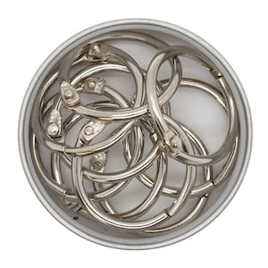 May include: A container of silver metal binder rings. The rings are in a variety of sizes and are arranged in a random pattern.