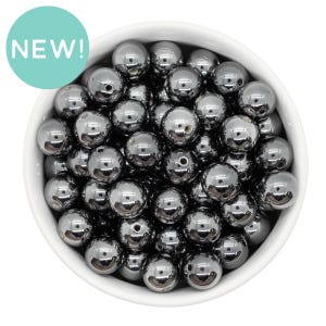 May include: A bowl filled with shiny, dark gray, round beads. The beads are smooth and have a reflective surface.