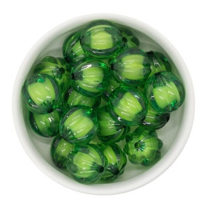 May include: A bowl filled with green, translucent, watermelon-shaped beads. The beads have a ribbed texture and are arranged in a random pattern.