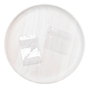 May include: Two clear plastic badge holders on a white wooden surface. The holders are rectangular and have a hole at the top for a lanyard.